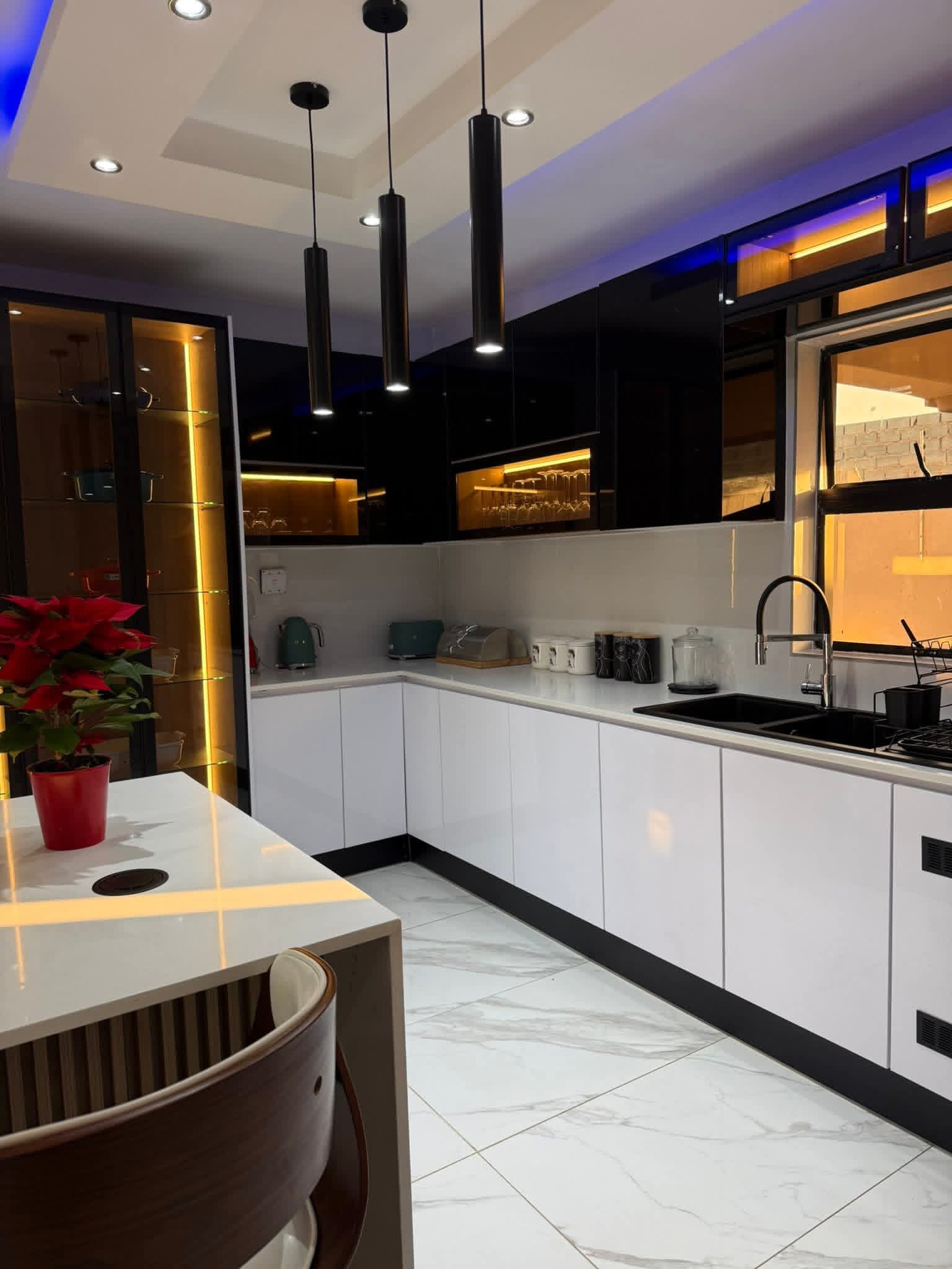 Gloss white and black kitchen with warm display lighting, marble floors and a breakfast island in Harare